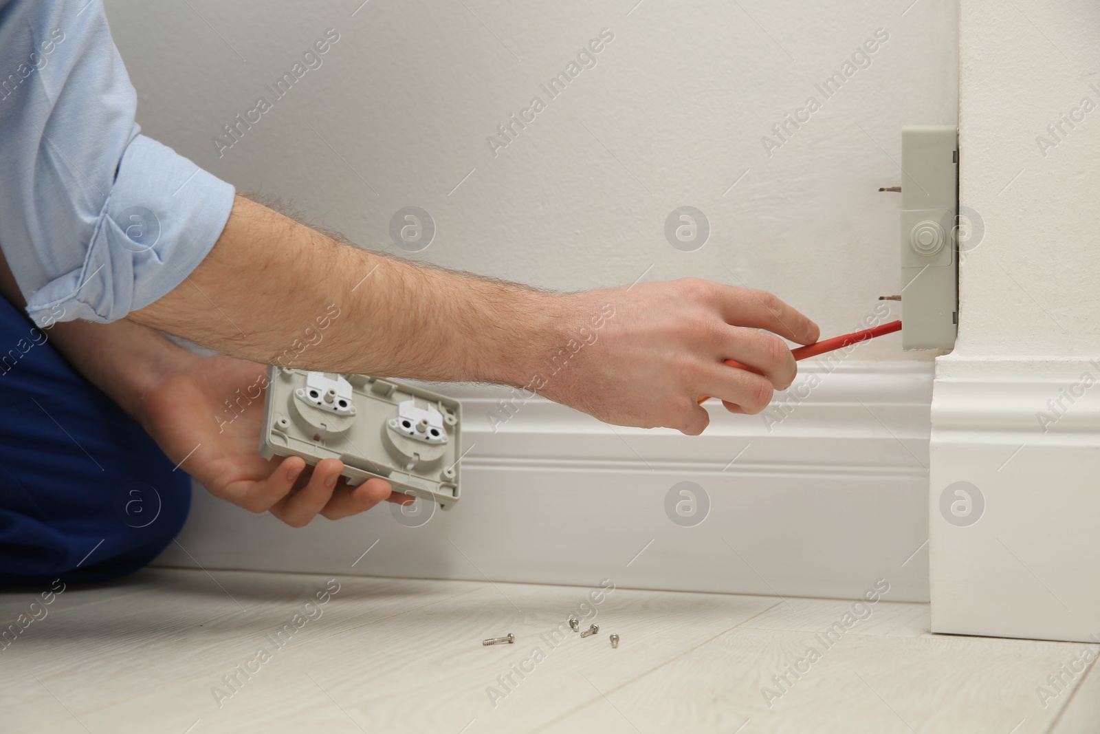 Photo of Electrician with screwdriver repairing power socket indoors, closeup