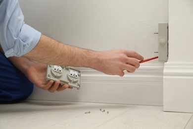 Photo of Electrician with screwdriver repairing power socket indoors, closeup