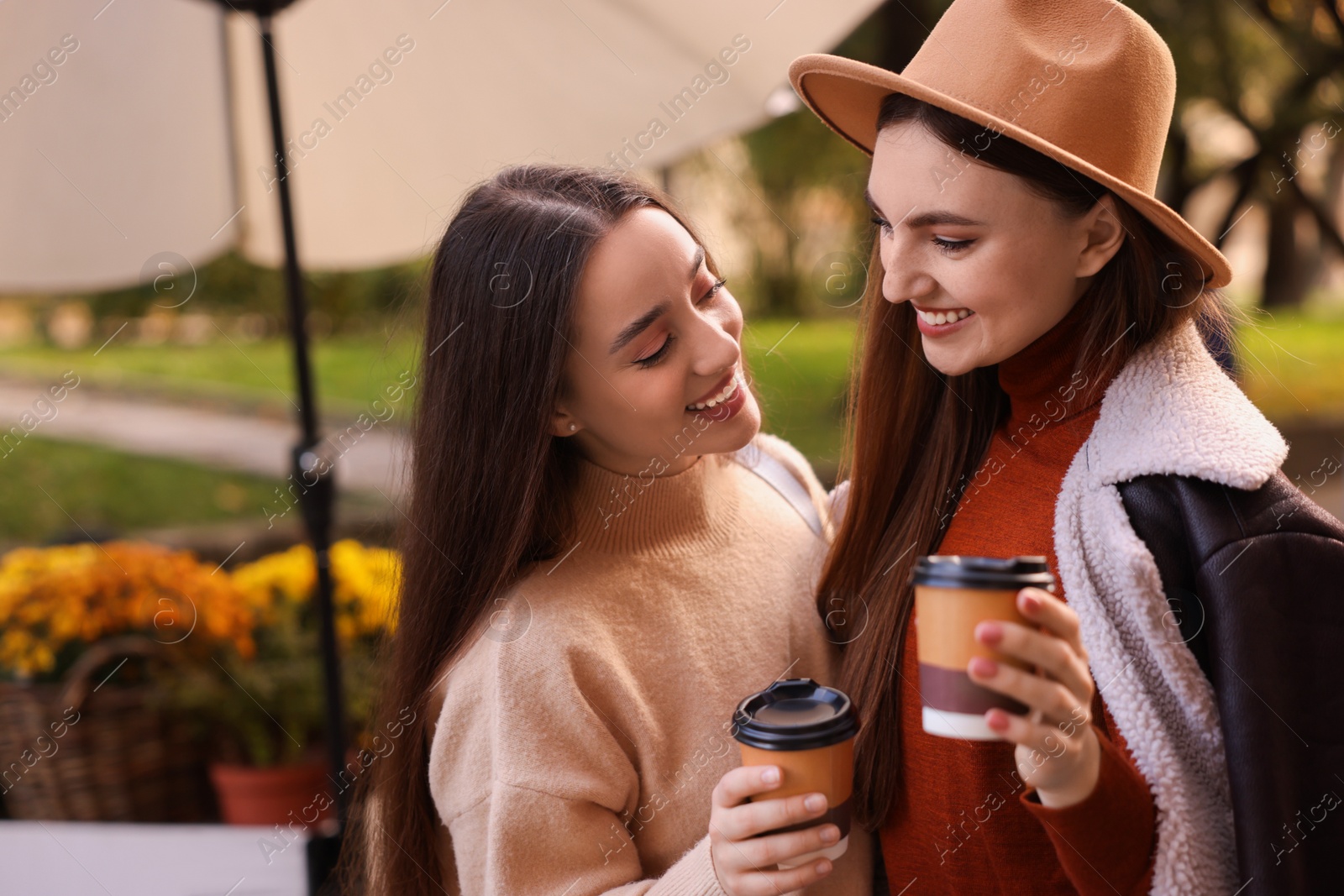 Photo of Happy friends with paper cups of coffee outdoors, space for text