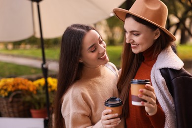 Photo of Happy friends with paper cups of coffee outdoors, space for text