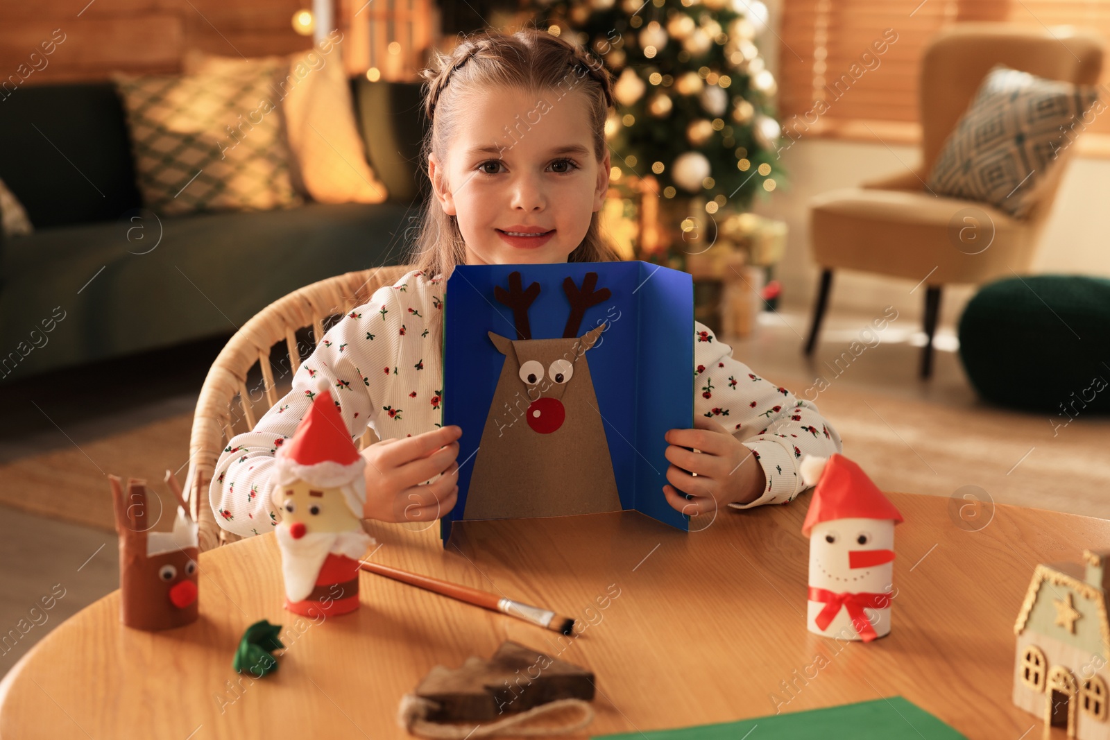 Photo of Cute child with Christmas greeting card at home