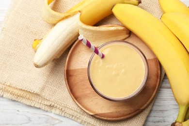 Photo of Glass of tasty banana smoothie with straw and fresh fruits on white wooden table, flat lay