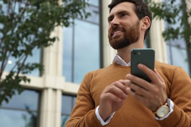 Handsome man with smartphone on city street, space for text