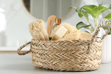 Photo of Natural loofah sponges and soap bar in wicker basket on table indoors, closeup