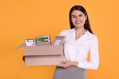 Photo of Happy unemployed woman with box of personal office belongings on orange background