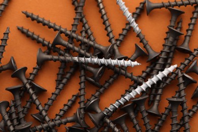 Photo of Many metal screws on orange background, flat lay