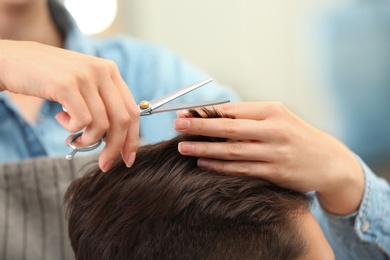 Photo of Barber making stylish haircut with professional scissors in beauty salon, closeup