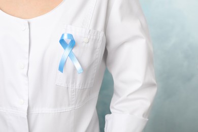 Doctor with light blue awareness ribbon on color background, closeup