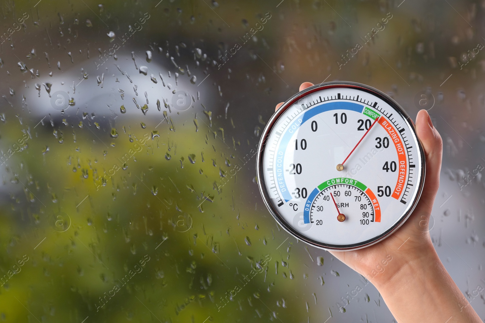 Image of Woman holding hygrometer with thermometer near window on rainy day, closeup. Space for text