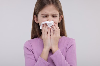 Sick girl with tissue coughing on light background