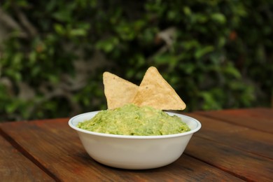 Photo of Delicious guacamole made of avocados with nachos on wooden table outdoors