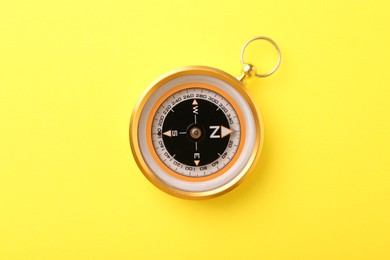 Photo of Compass on yellow background, top view. Navigation equipment