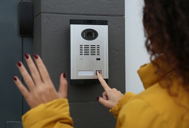 Photo of African-American woman ringing intercom while waving to camera near building entrance