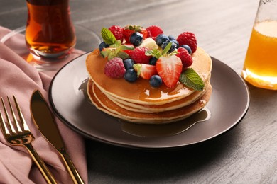 Photo of Delicious pancakes with fresh berries, honey and butter served on grey table, closeup