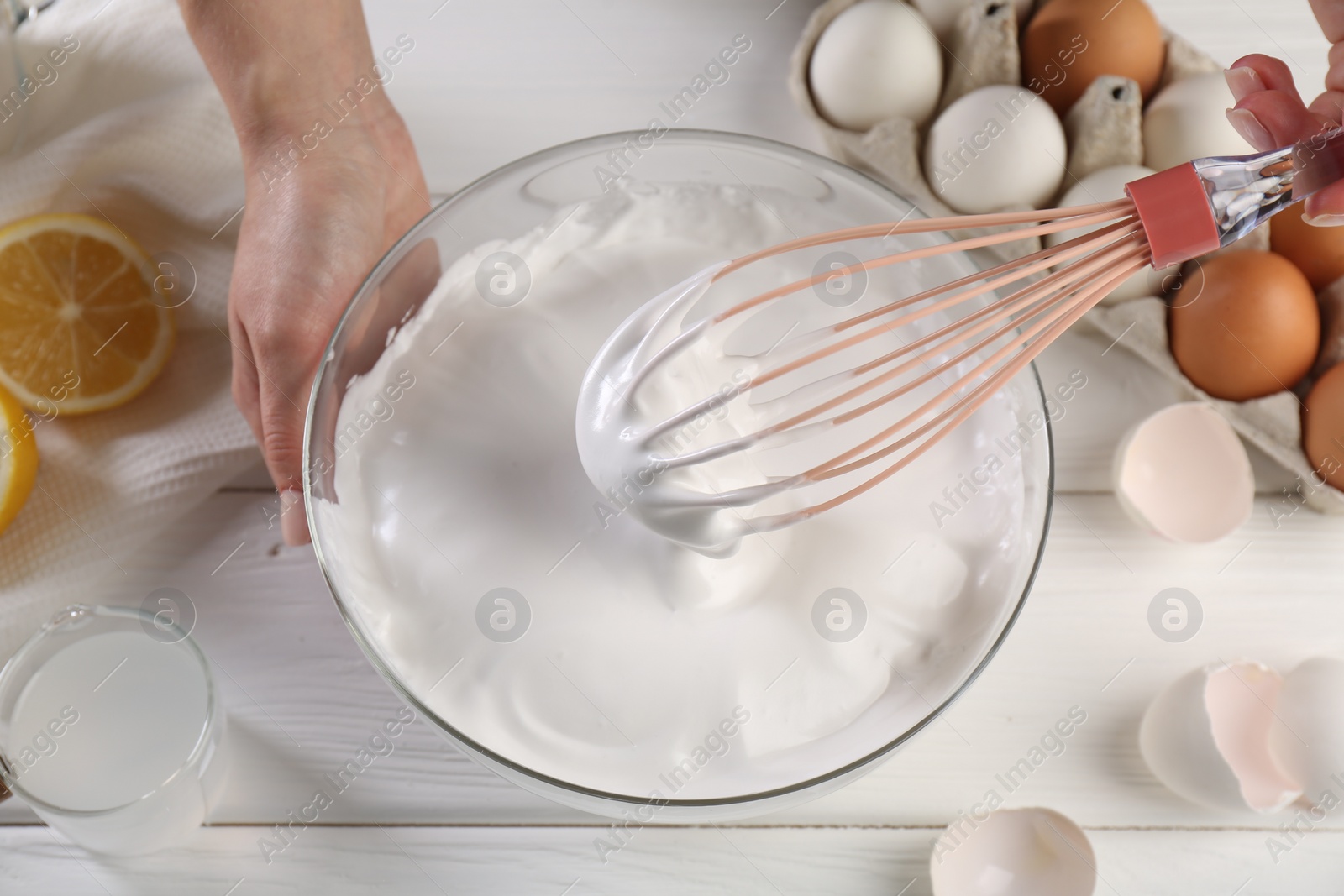 Photo of Woman making whipped cream with whisk at white wooden table, above view