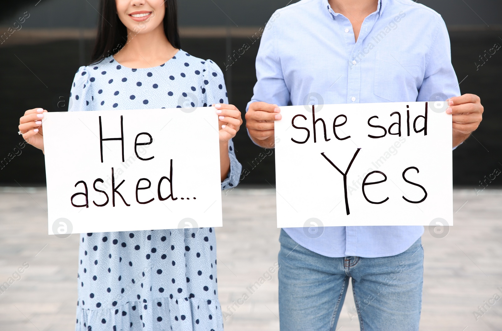 Photo of Lovely couple holding posters with text HE ASKED... SHE SAID YES after engagement outdoors, closeup