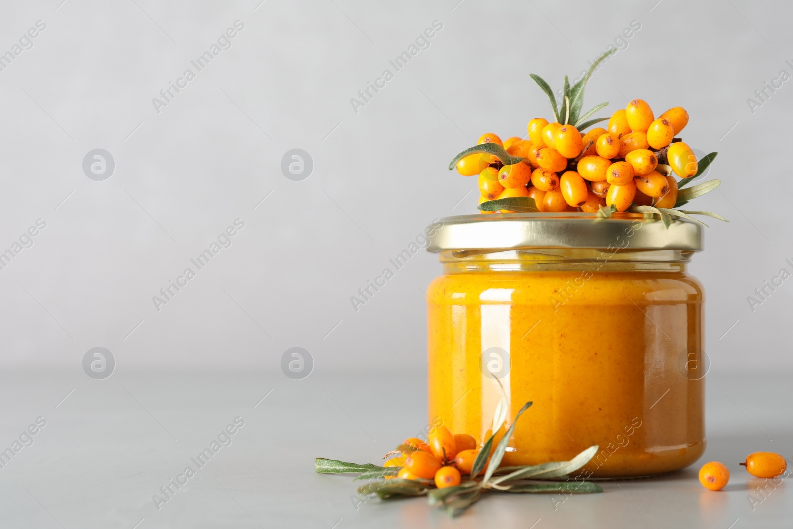 Photo of Delicious sea buckthorn jam and fresh berries on grey table. Space for text