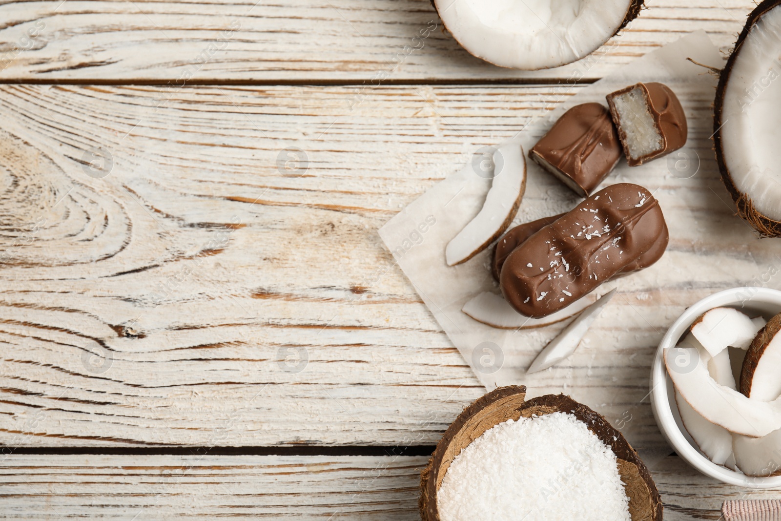 Photo of Delicious milk chocolate candy bars with coconut filling on white wooden table, flat lay. Space for text