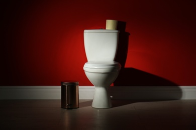 Toilet bowl with paper roll and trash bin in restroom