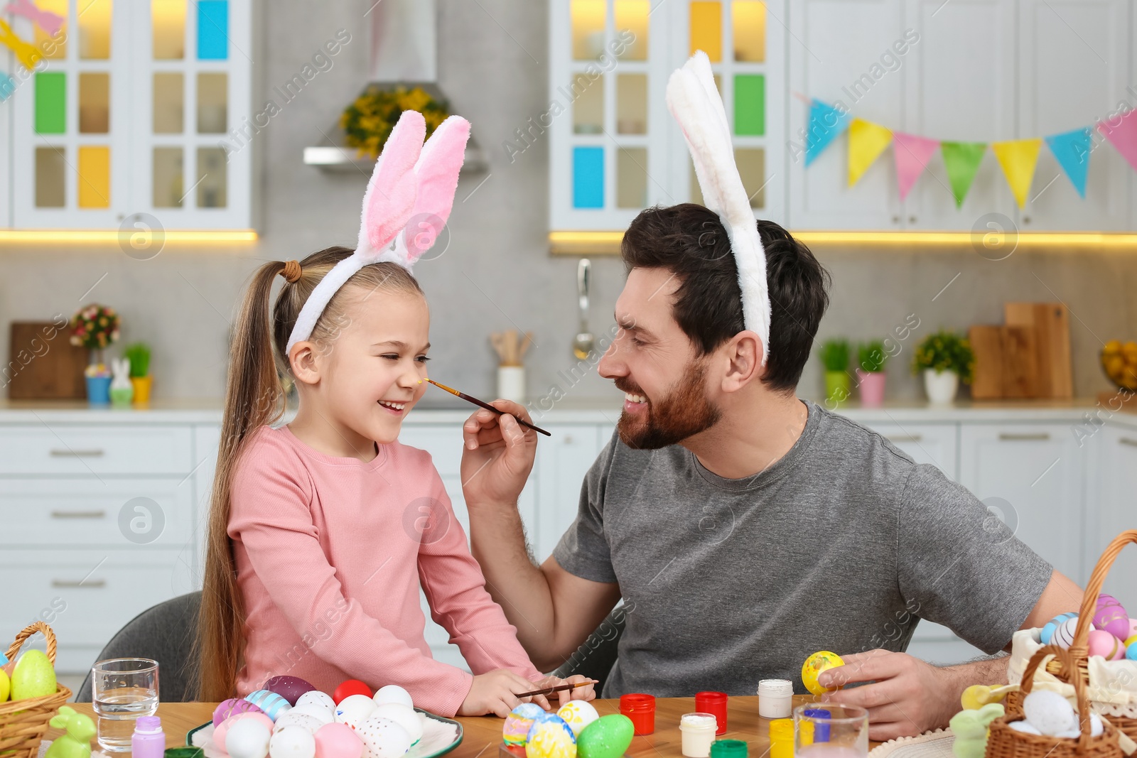 Photo of Father and his cute daughter having fun while painting Easter eggs at table in kitchen