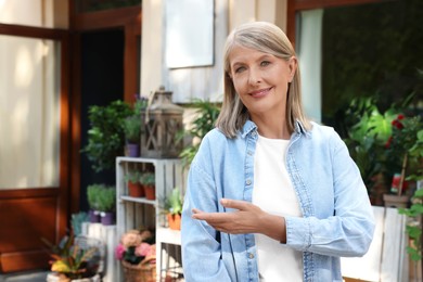 Photo of Happy business owner inviting to come into her flower shop outdoors, space for text