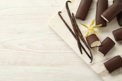 Photo of Glazed curd cheese bars, vanilla pods and flower on white wooden table, top view. Space for text