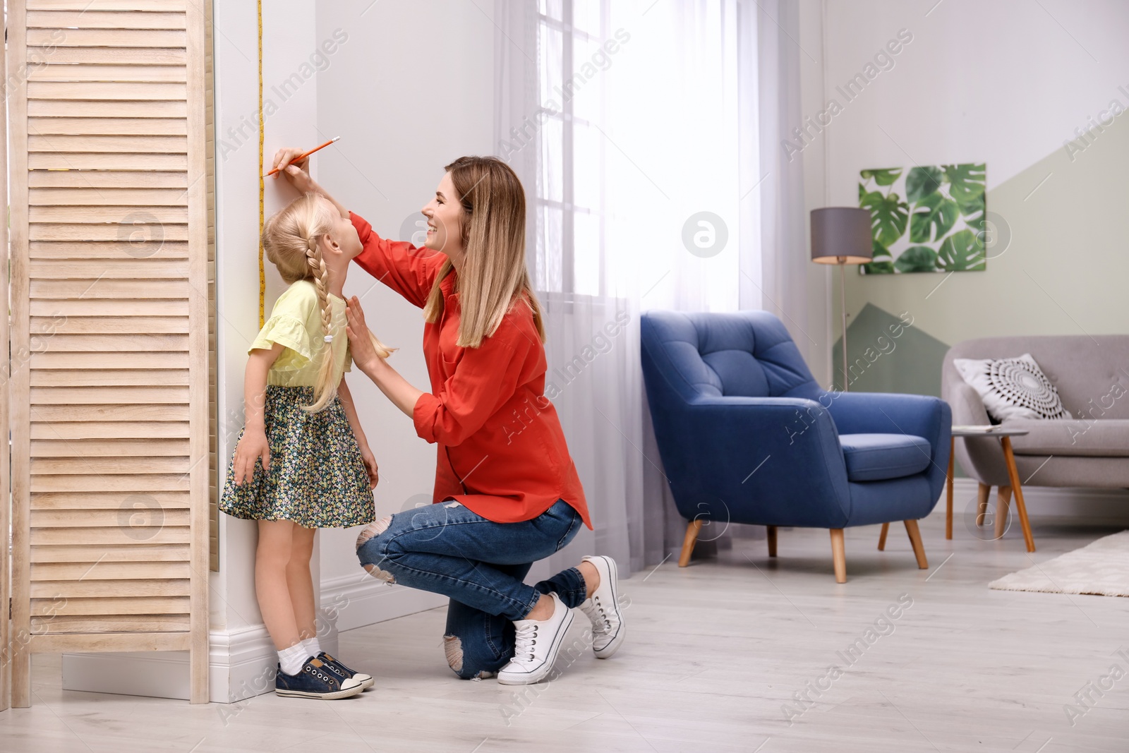 Photo of Young woman measuring her daughter's height at home