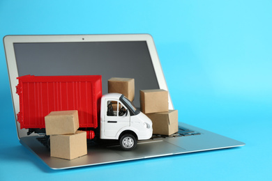 Photo of Laptop, truck model and carton boxes on light blue background. Courier service
