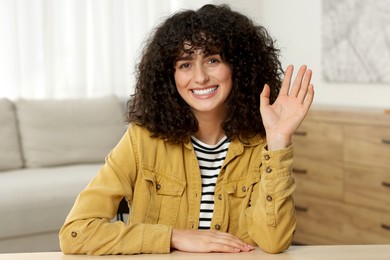 Happy woman waving hello at wooden table in room