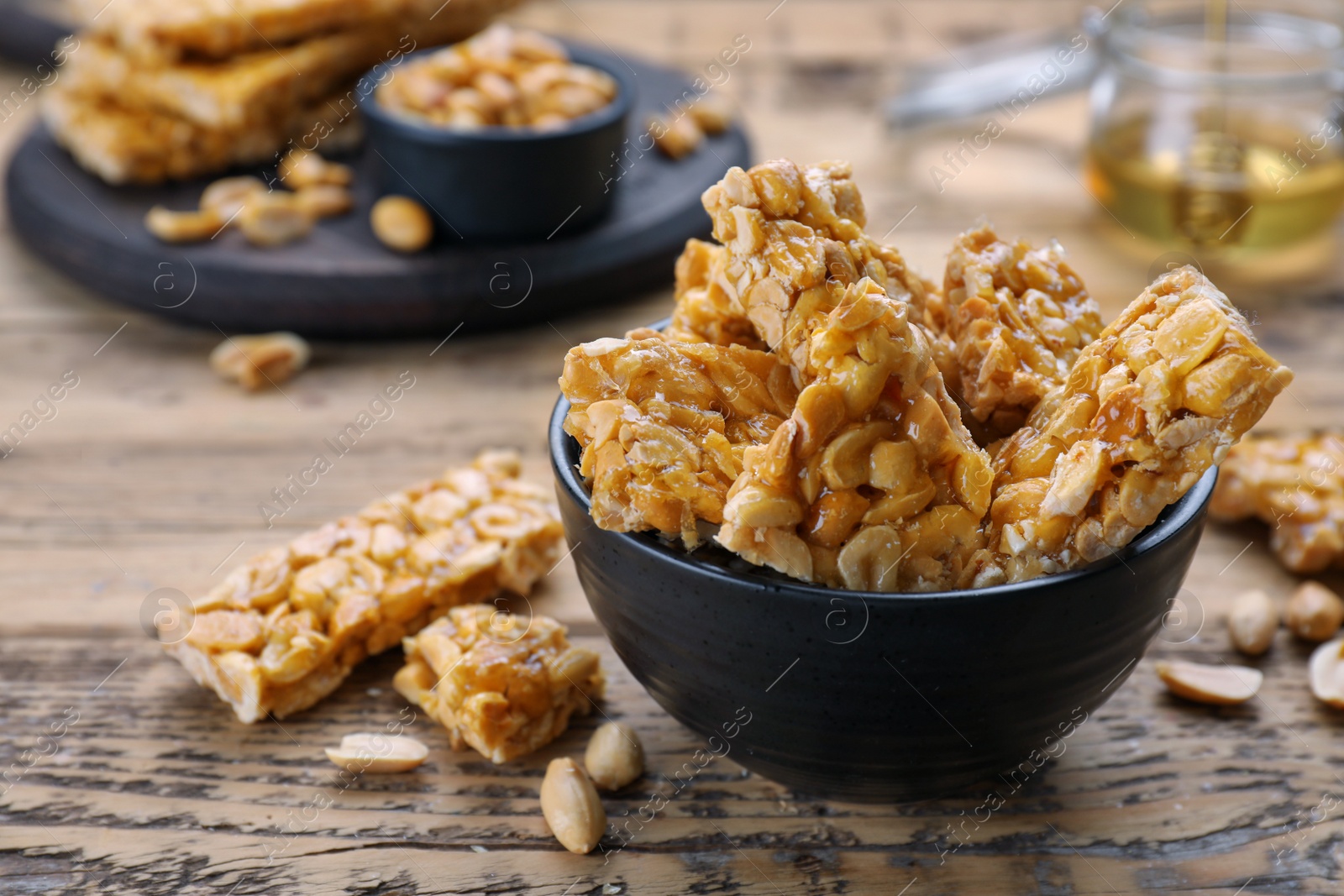 Photo of Delicious peanut kozinaki bars in bowl on wooden table, space for text