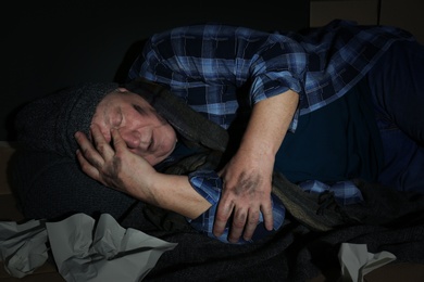 Poor senior man sleeping among garbage on floor