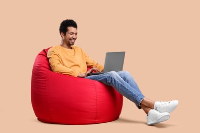 Happy man with laptop sitting on beanbag chair against beige background