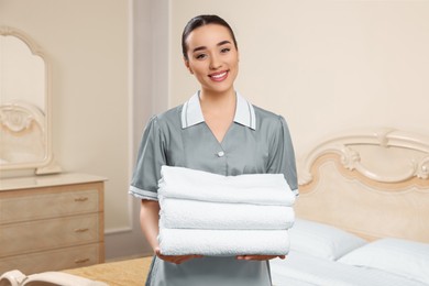 Photo of Young chambermaid holding stack of clean towels in hotel room