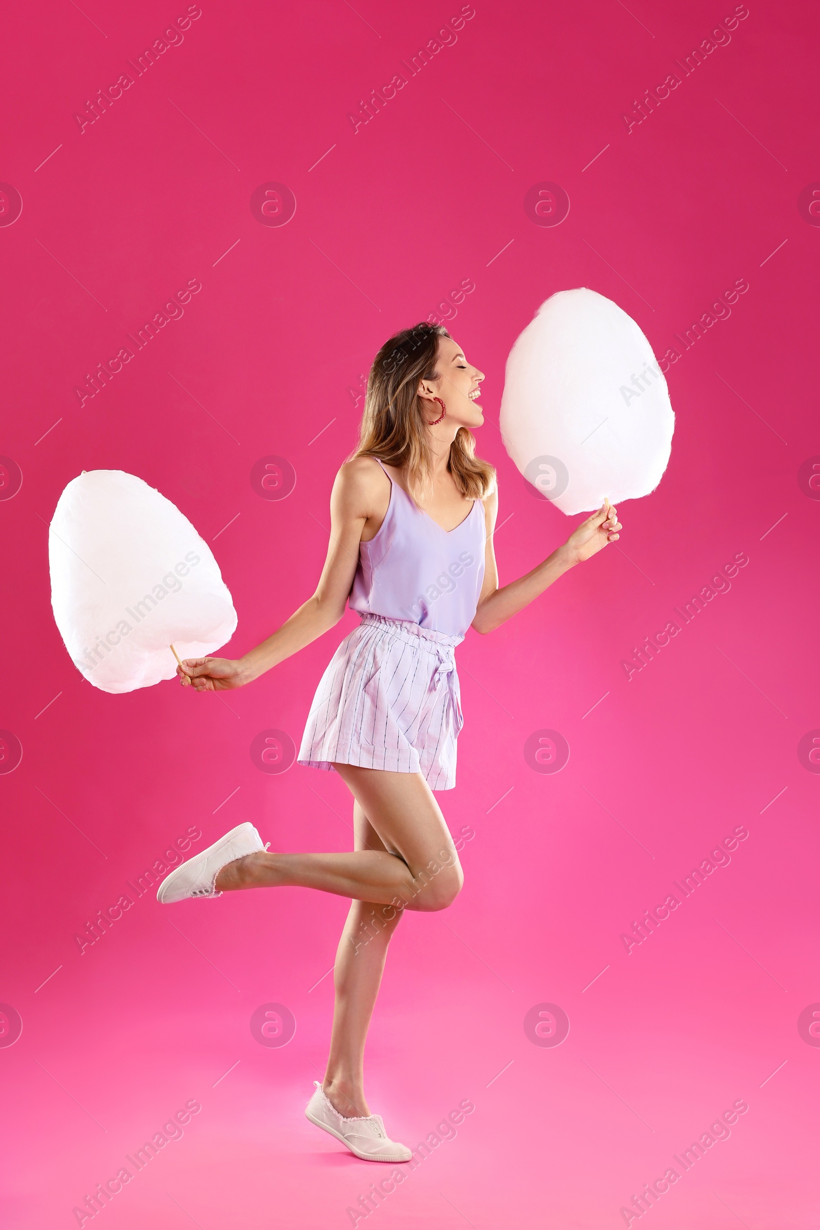 Photo of Happy young woman with cotton candies on pink background