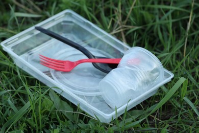 Photo of Used plastic tableware on grass outdoors, closeup. Environmental pollution concept