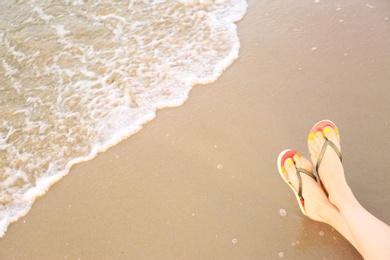 Photo of Closeup of woman with stylish flip flops on sand near sea, space for text. Beach accessories