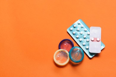 Condoms and birth control pills on orange background, flat lay and space for text. Choosing method of contraception