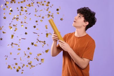 Photo of Happy teenage boy blowing up party popper on violet background