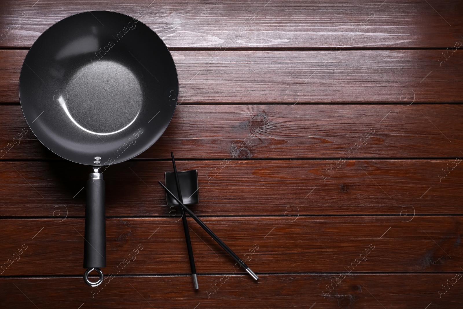 Photo of Empty iron wok and chopsticks on wooden table, flat lay. Space for text