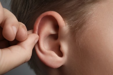 Photo of Boy touching his ear on grey background, closeup