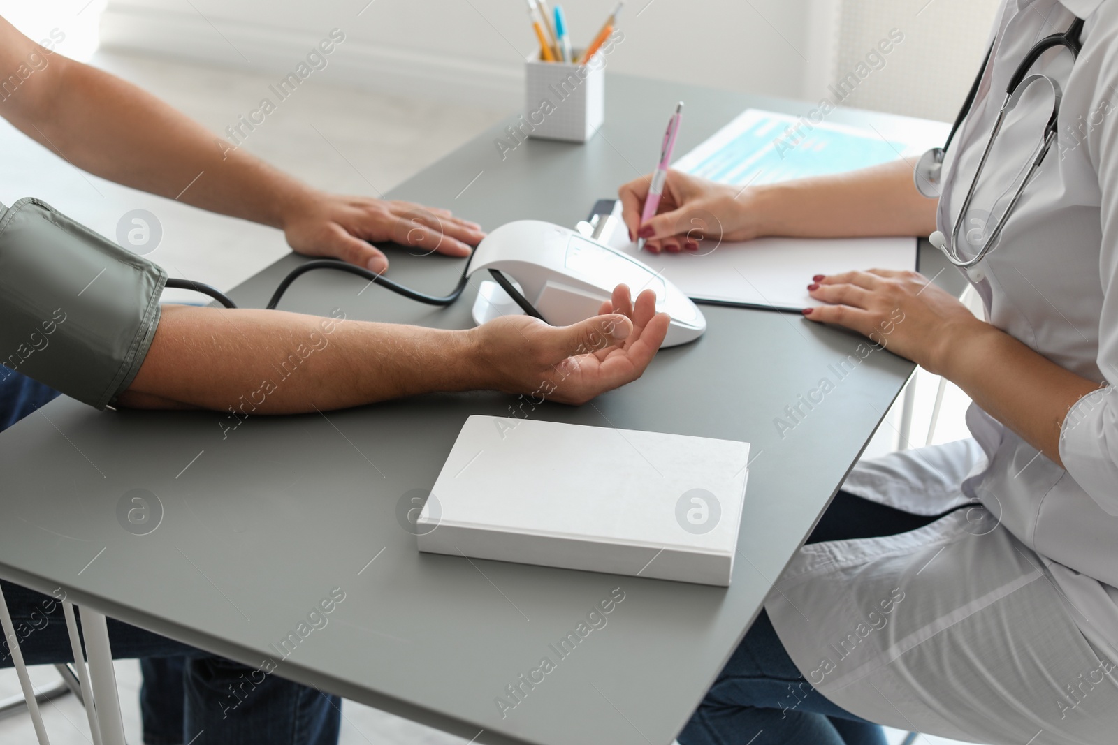 Photo of Doctor checking patient's blood pressure at table in office