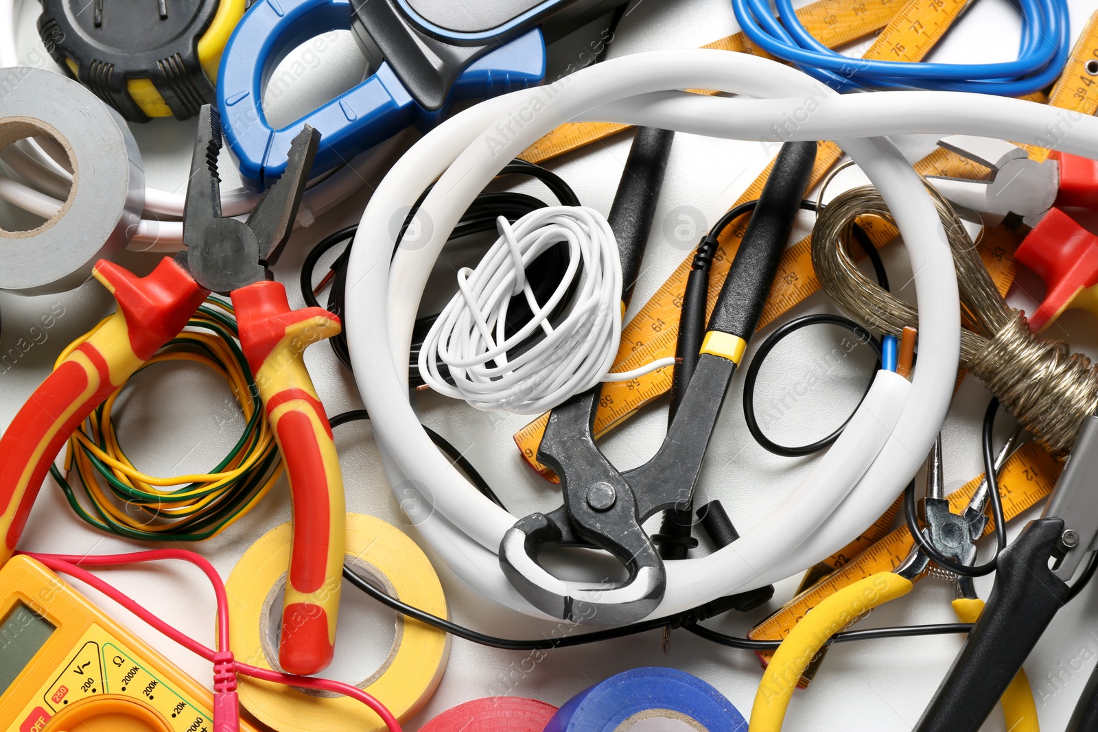 Photo of Different wires and electrician's tools on white table, flat lay