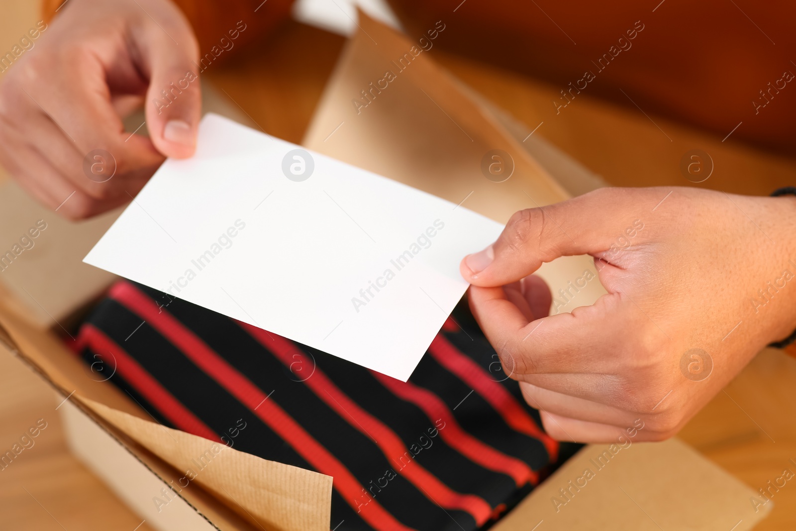 Photo of Young man holding greeting card near parcel with Christmas gift, closeup