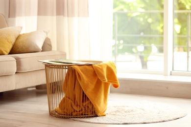 Metal basket with yellow blanket in modern room, space for text. Idea for interior design