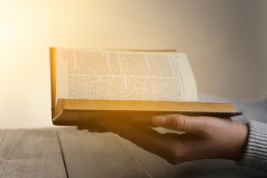 Photo of Woman reading Bible at wooden table, closeup