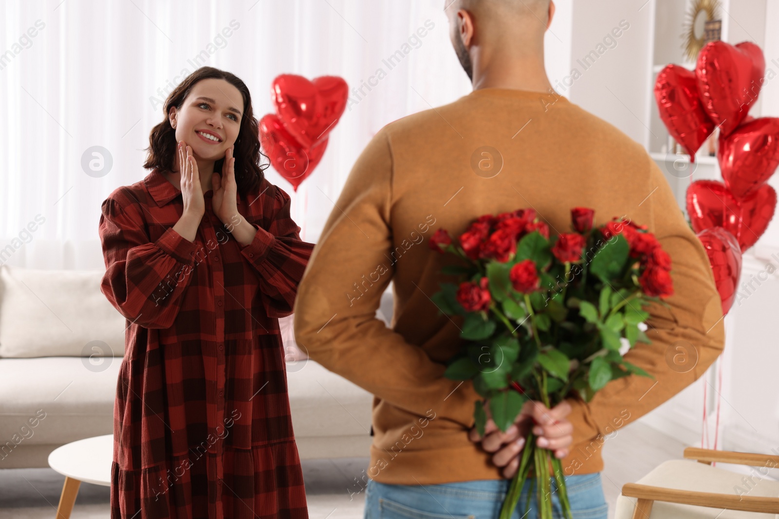 Photo of Man hiding bouquet of red roses for his beloved woman at home. Valentine's day celebration