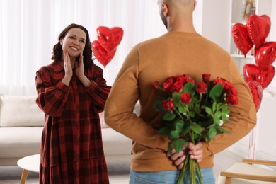 Man hiding bouquet of red roses for his beloved woman at home. Valentine's day celebration