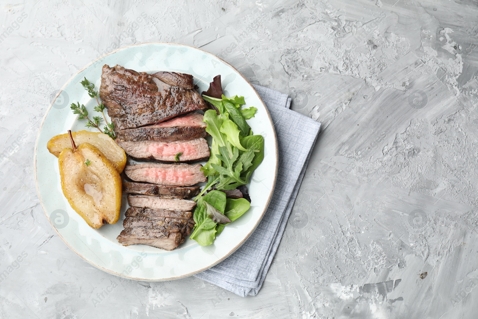 Photo of Delicious roasted beef meat, caramelized pear and greens on light textured table, top view. Space for text