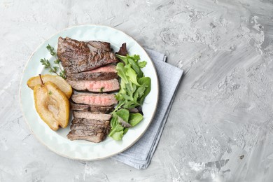 Photo of Delicious roasted beef meat, caramelized pear and greens on light textured table, top view. Space for text