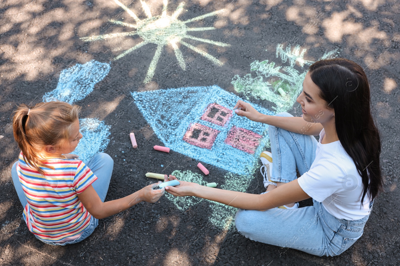 Photo of Cute little child and her mother drawing with colorful chalks on asphalt, above view